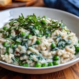 Close-up of vibrant green risotto with sweet peas and Parmesan, showcasing rich texture and fresh herb garnish.  