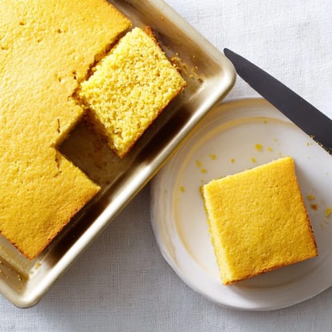 A slice of fluffy Cornbread showing a moist, tender crumb, served on a rustic plate ready for a generous spread of honey butter.