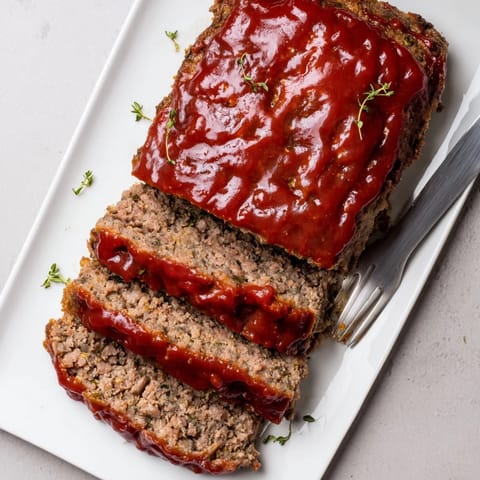 Slices of juicy Classic Meatloaf served alongside creamy mashed potatoes and steamed green beans.
