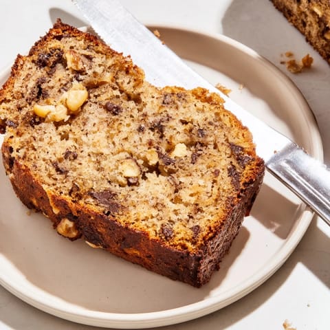 A warm slice of banana bread with melting butter and chocolate chips on a plate next to a coffee mug.