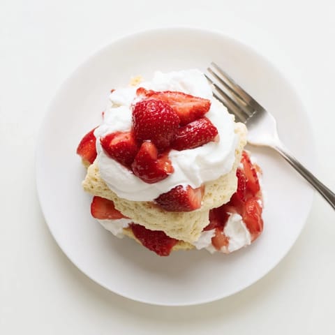 Strawberry Shortcake served in a glass, showing red berry syrup soaking into tender biscuits topped with fresh cream.
