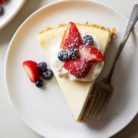 Perfectly set New York Cheesecake slice topped with sweet berry compote and fresh mint on a white dessert plate.