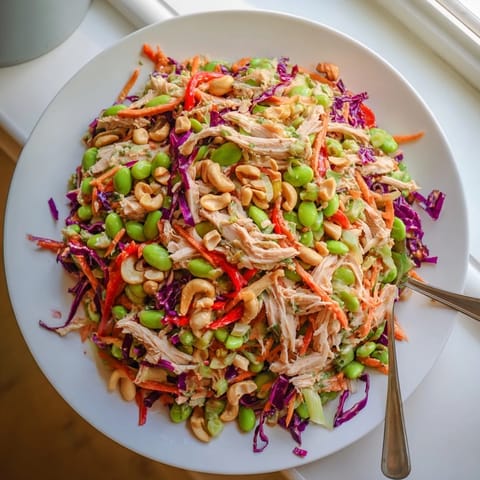 A close-up of Edamame Crunch Chicken Salad with shredded chicken, crisp cabbage, carrots, and edamame in a zesty ginger dressing.