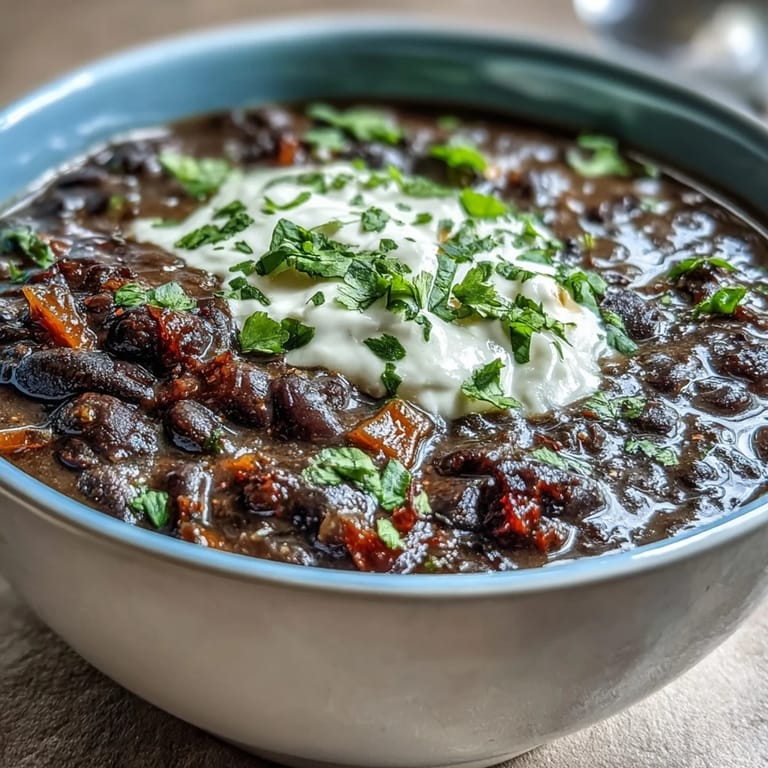 Close-up of creamy Black Bean Soup with a swirl of sour cream and a side of lime wedges.