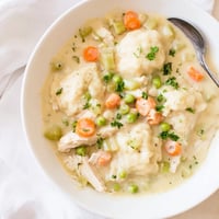 Steaming bowl of homemade Chicken and Dumplings, featuring tender chicken, carrots, and peas in a rich creamy broth topped with fluffy dumplings.